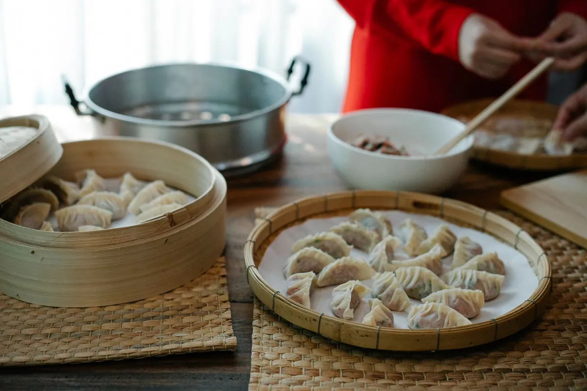 Raviolis vapeur jiaozi dressés en éventail dans un panier en bambou, pâte plissée légèrement translucide, servis avec une sauce au vinaigre noir et soja