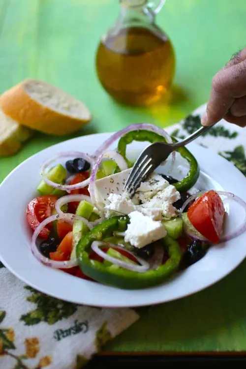 Salade grecque horiatiki dans un plat en terre cuite, avec tomates, concombre, poivron, oignon rouge, olives de Kalamata et un bloc entier de feta arrosé d'huile d'olive et d'origan.