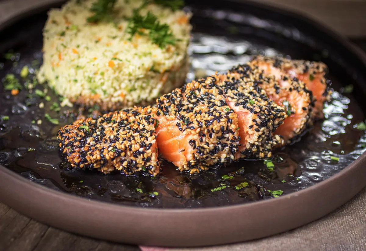 Pavé de saumon teriyaki grillé, marqué au gril et nappé d'une sauce soja brune et brillante, parsemé de ciboule ciselée et servi sur une assiette allongée.