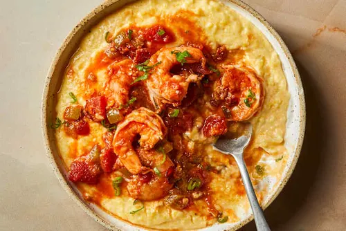 Assiette de shrimp and grits : crevettes sautées au paprika fumé et à l'ail sur une semoule de maïs crémeuse au cheddar, garnie d'oignon nouveau et de persil frais.
