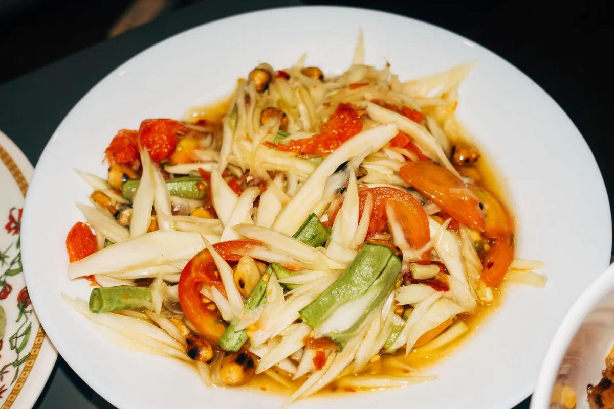Salade thaïe som tam de papaye verte pilée au mortier, avec haricots longs, tomates cerises, cacahuètes concassées et crevettes séchées.