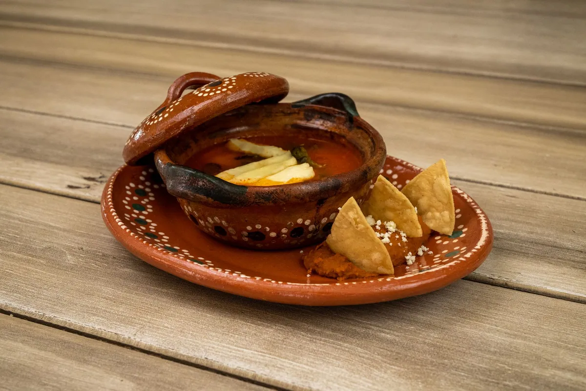 Bol de sopa de tortilla mexicaine : bouillon de tomate garni de lanières de tortillas frites, tranches d'avocat, queso fresco émietté, crème et piment pasilla, parsemé de coriandre fraîche.