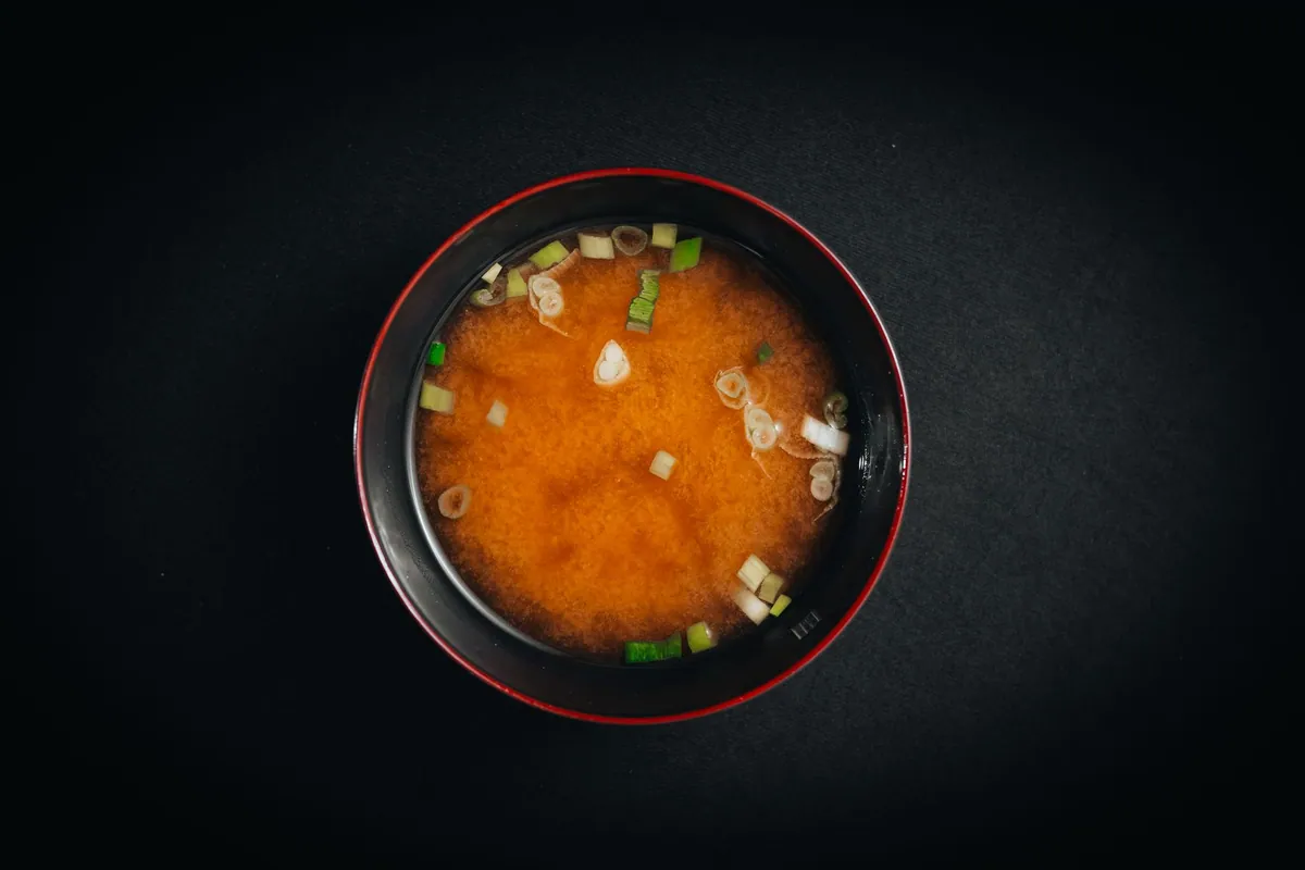 Bol de soupe miso japonaise avec tofu soyeux, algues wakame et ciboule ciselée, servi dans un bol laqué traditionnel.
