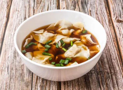 Bols de soupe won-ton cantonaise avec raviolis porc-crevette, pak choï et bouillon de volaille au gingembre, parsemés d'oignon nouveau.