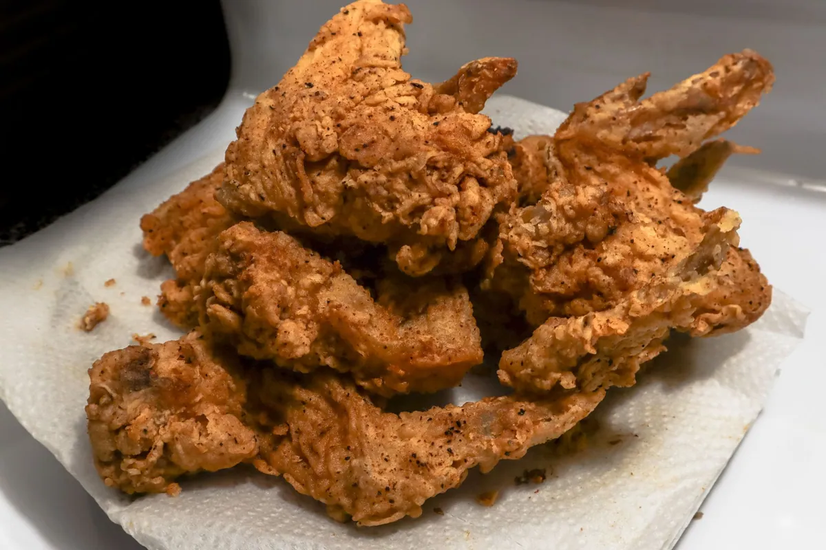 Morceaux de poulet frit du Sud à la croûte dorée et craquante, dressés sur une grille avec du pain de maïs et des pickles en accompagnement.