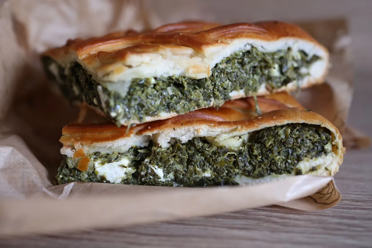 Spanakopita grecque dorée et croustillante, tourte à la pâte filo garnie d'épinards, de feta et d'herbes fraîches, part découpée laissant apparaître les couches feuilletées.