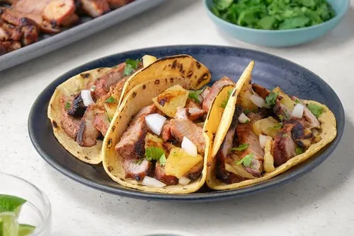Tacos al pastor garnis de porc mariné à l'achiote grillé, ananas caramélisé, oignon et coriandre, sur tortillas de maïs chaudes