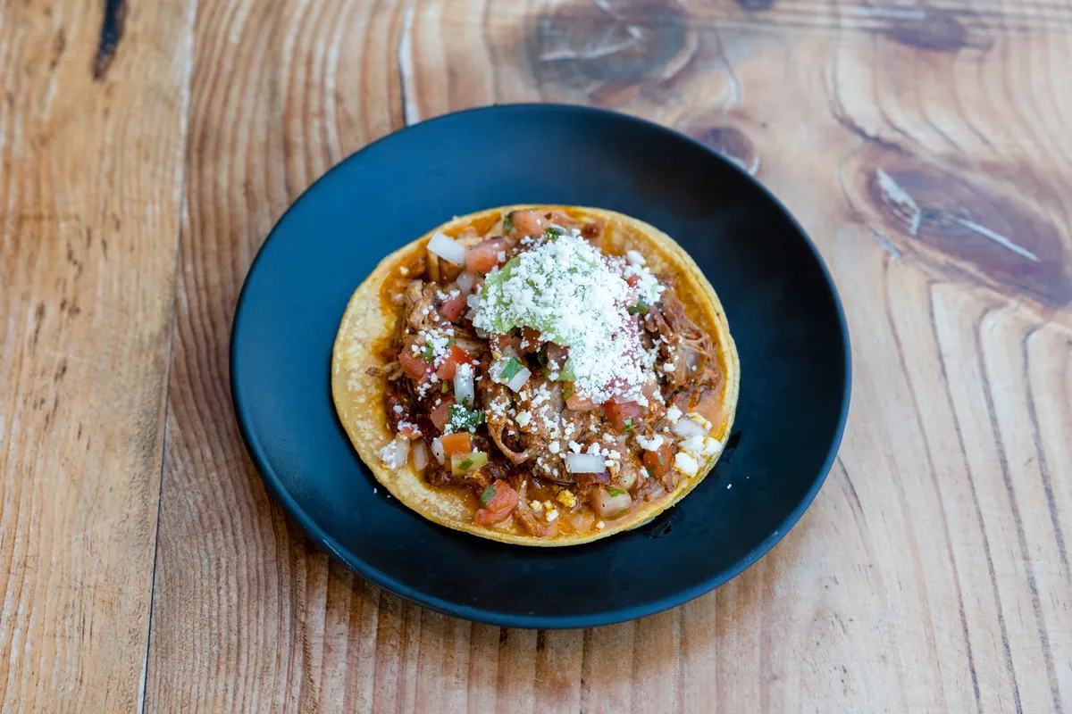 Tostadas de tinga de pollo garnies de poulet effiloché à la sauce tomate-chipotle, crème, avocat en tranches, queso fresco émietté et coriandre fraîche
