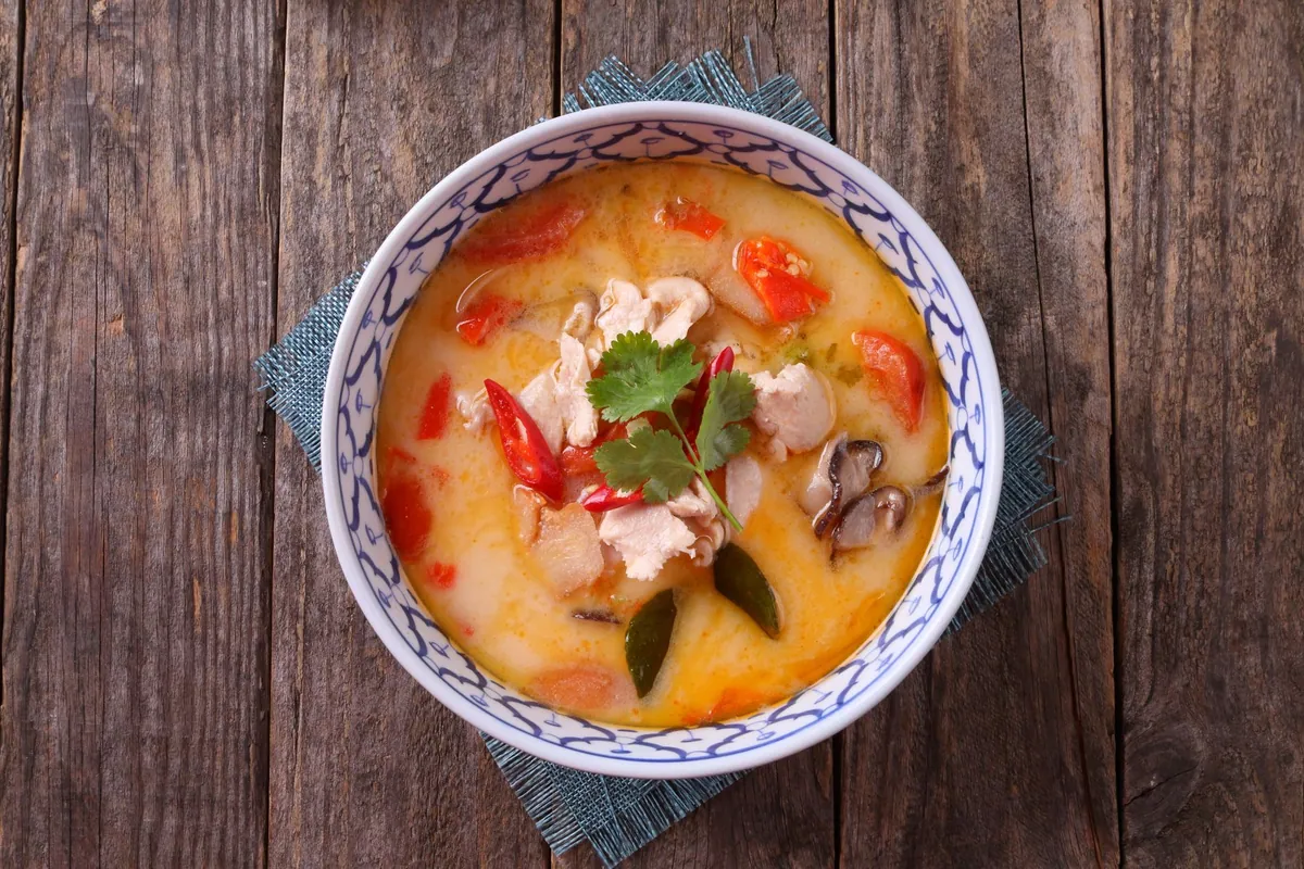 Bol de tom kha kai, soupe thaïlandaise crémeuse au lait de coco, poulet effiloché, champignons, citronnelle et coriandre fraîche, servie chaude avec un quartier de citron vert.