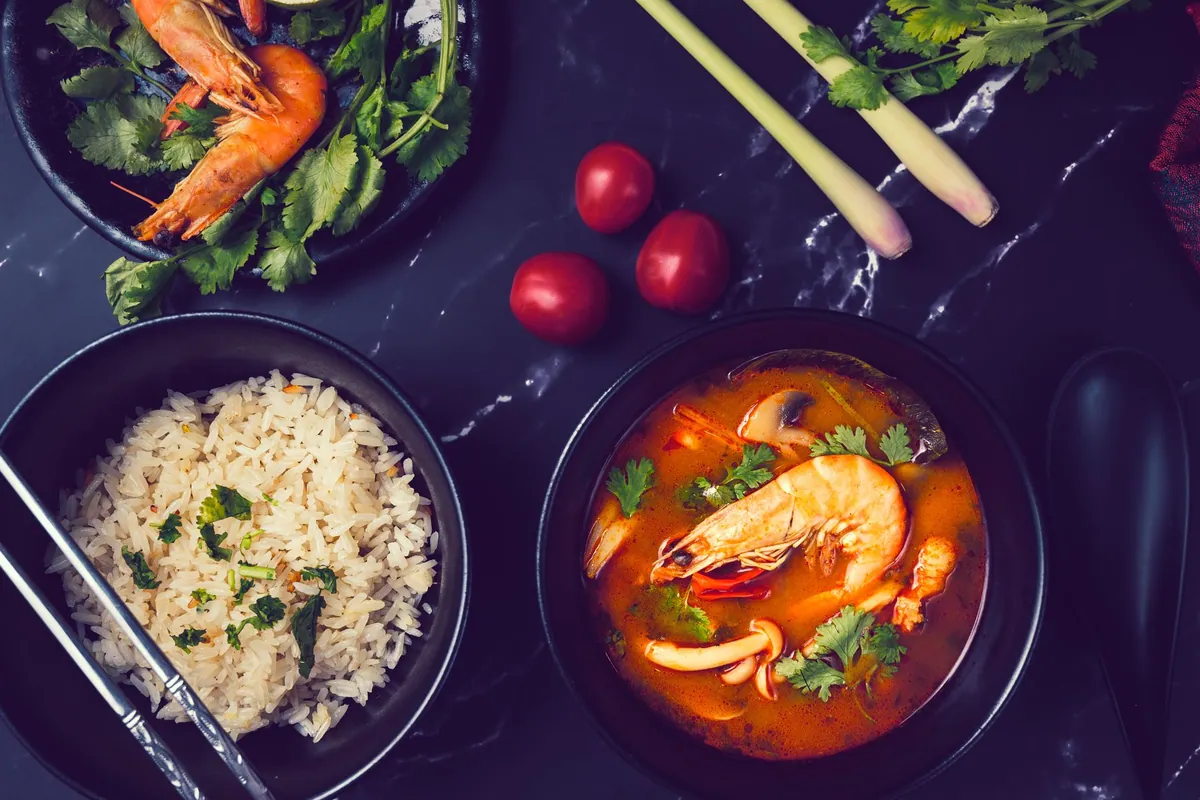 Bol de tom yum goong fumant avec crevettes roses, champignons de paille, citronnelle et coriandre fraîche dans un bouillon épicé orangé.