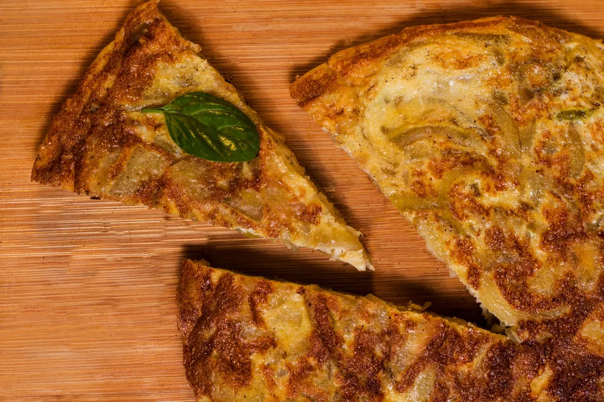 Tortilla española épaisse, coupée en parts triangulaires, pommes de terre fondantes et cœur crémeux, servie sur une assiette en bois.