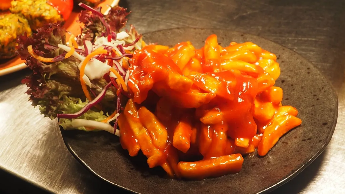 Tteokbokki coréen, gâteaux de riz nappés d'une sauce rouge au gochujang, avec galettes de poisson, oignons nouveaux et œuf dur, servi fumant dans une poêle.